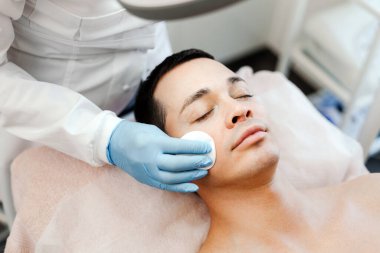 Yakından doktor, kozmetik uzmanı yakışıklı genç hastaya estetik ameliyatlar yapıyor, yüz derisini temizliyor. Kozmetik bilimi, gençleştirme, sivilce tedavisi kavramı