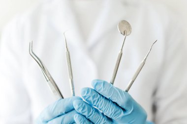 Beyaz önlüklü profesyonel dişçi doktoru steril diş aletleri tutan lateks eldivenli, seçici odaklı, yakın plan. Ekipman kavramı, diş bakımı
