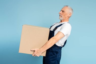 Mavi duvar arka planında ağır dolap kutusu taşıyan yorgun kurye. Nakliye şirketi, taşıma hizmeti kavramı