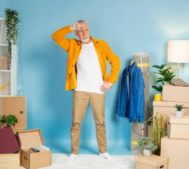 Düşünceli adam yeni evdeki eşyalarla birlikte kutuların yanında duruyor. Konutların yeniden dekore edilmesi veya onarılması, ev sahiplerinin portresi, yaşlı vatandaş için banka kredisi, tadilat kavramı