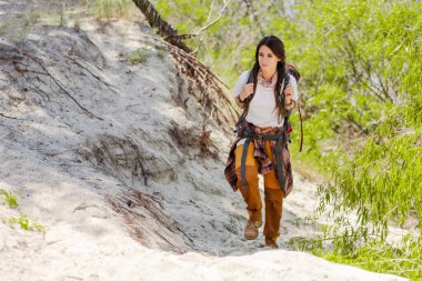 Sırt çantalı gezgin kadın sıcak mevsimde yürüyüş yaparken kumlu yüzeyde geziniyor. Tatil ve macera konsepti