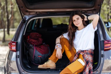 Güzel, genç bir kadın arabanın bagajında oturmuş, doğa yürüyüşüne çıkmaya hazırlanıyor. Macera konsepti