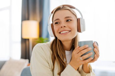 Genç bir kadın evde kahveyle müzikten zevk alıyor, mutlu bir şekilde gülümsüyor. Kablosuz kulaklıklar onu bir müzik listesine bağlıyor. Gününde keyifli bir ara veriyor.