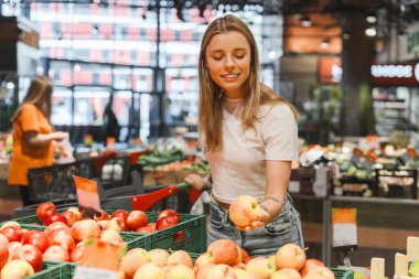 Kadın, organik ürünlerle sağlıklı bir yaşam tarzını yansıtan taze kırmızı elmaları marketten seçiyor. Yiyecek, alışveriş konsepti
