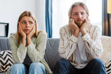 Üzgün, sıkılmış bir çift evdeki rahat bir koltukta oturur ve yorgun, hayal kırıklığına uğramış vücut dilleriyle ilişki belirtileri gösterir.