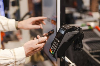 Müşteri akıllı telefonunu bir ödeme terminalinin üzerinde tutuyor. NFC teknolojisini kullanarak marketteki bakkaliyesine ulaşılamaz bir ödeme yapıyor.