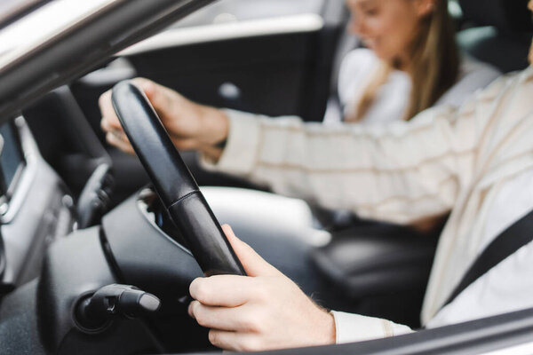 Two professionals happily driving in a luxurious car through the city on a sunny day, focused on the road ahead. Comfortable and safe interior, hands on the steering wheel, blurred urban background