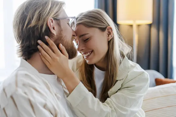 stock image Young couple enjoying a quiet moment at home, embracing and smiling with love and affection in a cozy living room bathed in natural light. Love concept