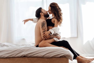 Tutkulu, genç ve seksi bir çiftin portresi. Yatakta oturmuş öpüşüyor, sarılıyor. Cinsellik, tutku konsepti