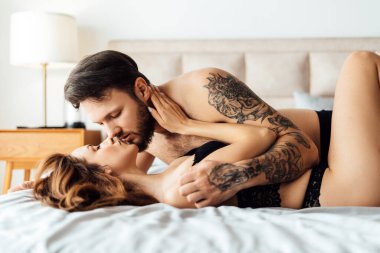 Genç ve seksi sakallı bir adam yatakta uzanıp onu öperken seksi bir kadına sarılıyor. Cinsellik, tutku konsepti