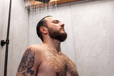 Sakallı seksi çıplaklık portresi. Su damlalarının altında duran dövmeli yakışıklı adam. Duş alıyor. Çıplaklık, cinsellik kavramı