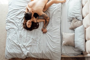 Yatak odasında bir kadının boynunu öpen ve el ele tutuşan genç bir çiftin çıplak portresi. Cinsellik, tutku konsepti