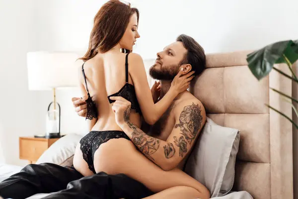 stock image Portrait of passionate young lovers in underwear embracing and kissing, sitting on the bed, looking each other. Sexuality, passion concept