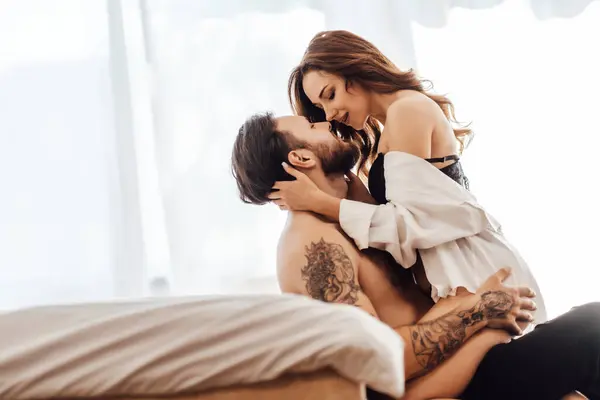 Zarif dantelli iç çamaşırı giyen genç bir kadının portresi. Yatağın yanında oturan adamı öpüyor. Cinsellik, tutku konsepti