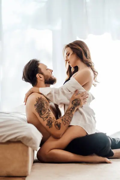 Genç bir adam ve kadının birbirine sevgiyle bakan dikey portresi. Yatak odasında yerde oturuyor. Cinsellik, tutku konsepti