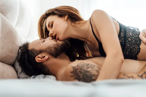 Siyah dantelli iç çamaşırlı çekici bir kadının portresi erkek arkadaşını öpüyor, yatağa uzanıyor, gözlerini kapatıyor cinsellik, tutku konsepti.