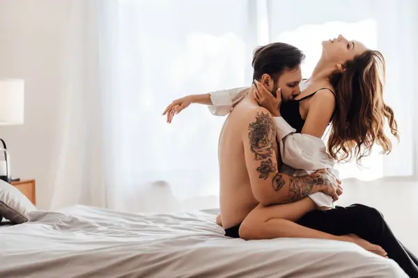 stock image Side view portrait of passionate bearded young man without clothing kissing sexy woman sitting on bed, embracing. Sexuality, passion concept