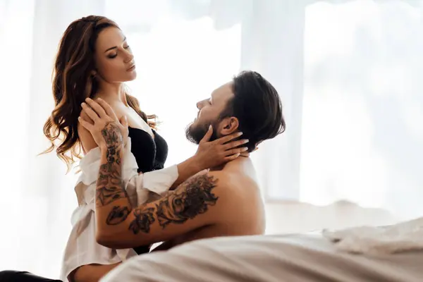 Yatak odasında yerde oturan yakışıklı kaslı adama seksi iç çamaşırlı, baştan çıkarıcı genç bir kadının portresi. Cinsellik, tutku konsepti