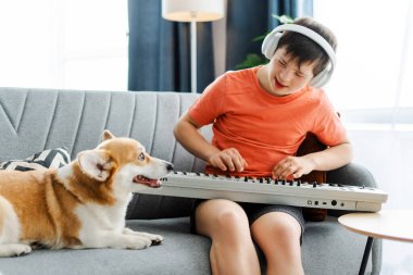 Genç bir çocuk, Down sendromlu bir genç köpekle klavye sentezleyicisinde müzik çalıyor, evdeki rahat kanepede oturuyor. Hobi konsepti