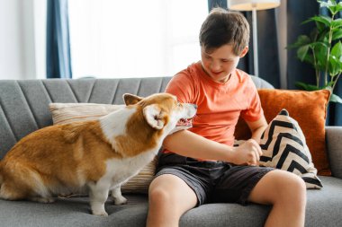 Down sendromlu mutlu genç evinde rahat bir kanepede oturmuş evcil Corgi 'siyle oynuyor. Arkadaşlık, aşk, hayvan konsepti.