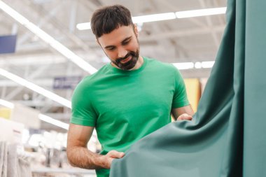 Dekor bölümünde perde seçen gülümseyen bir gencin portresi. Alışveriş konsepti