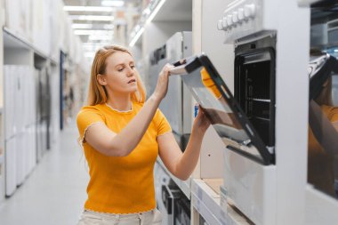 Mobilya dükkanında mutfak için yeni modern fırını seçen güzel bir kadının portresi. Alışveriş konsepti