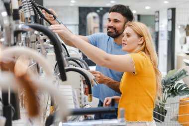 Genç ve mutlu bir çiftin portresi. Tesisatçı dükkanında yeni bir mutfak musluğu seçiyor. Alışveriş konsepti