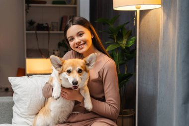 Güzel kız, genç kız evdeki rahat bir kanepede Corgi 'sine sarılıp samimi bir arkadaşlık anında sıcaklık ve sevgi saçar. Arkadaşlık, aşk, hayvan konsepti.