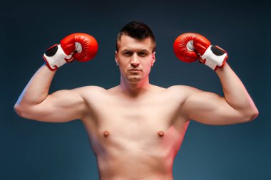 Kendine güvenen boksör, güçlü kollarını kırmızı eldivenlerle mavi bir arka plana yaslar, azim ve sağlığa bağlılığını gösterir.