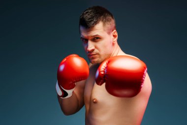 Etkileyici kasları olan kararlı erkek boksör spor salonuna güçlü bir yumruk atar, güç ve odaklanma yayar. Ciddi ifadesi ve kırmızı eldivenleri spora olan bağlılığını gösteriyor.