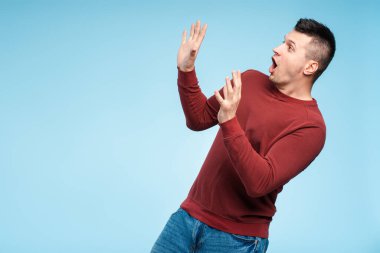 Adam korkmuş görünüyor, ellerini kaldırıyor, gözleri korku ve endişe içinde. Atmosfer gergin, panik ve korku uyandırıyor.