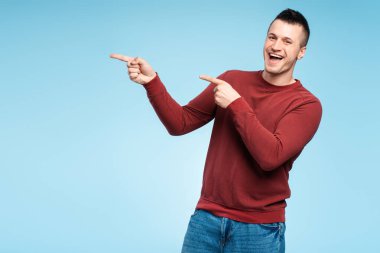 Orta yaşlı gülümseyen bir adam işaret parmağını metin ve logo için fotokopi alanına doğrultuyor. Pankart, panorama. Mavi arka planda izole edilmiş. Alışveriş konsepti