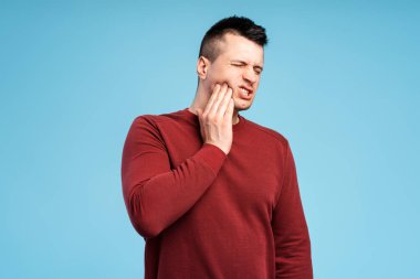 Diş sorunları. Yaralı yanağa baskı yapan sağlıksız bir adamın portresi, akut diş ağrısı, periodontal hastalık, çürük ya da mavi arka planda izole edilmiş çene ağrısı. Diş Konsepti