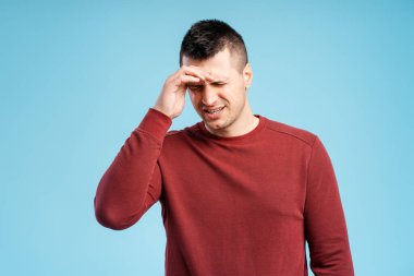 Orta yaşlı bir adam acıdan alnına dokunuyor, baş ağrısı mavi arka planda tek başına duruyor. Sağlık hizmeti kavramı