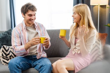 Mutlu çift modern bir oturma odasındaki rahat koltuklarında kahve içip, sabah ışığında konuşup, gülümsüyor. İlişki kavramı