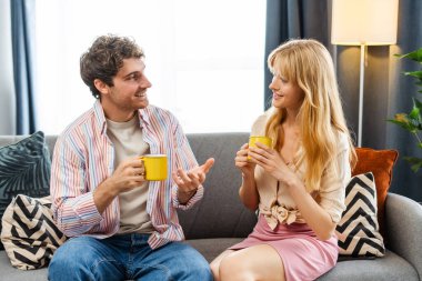 Genç çift evlerinde birlikte kaliteli zaman geçiriyorlar, rahat koltuklarında oturup, kahvelerini yudumluyor ve birbirlerinin arkadaşlığından keyif alıyorlar.