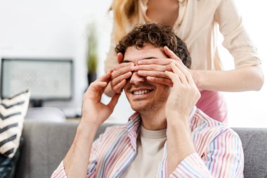 Yakışıklı genç adam kız arkadaşından sürpriz bekliyor, elleriyle gözlerini kapatıyor, evdeki kanepede oturuyor. İlişki kavramı