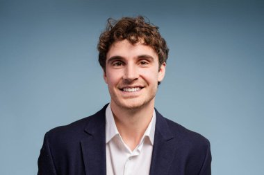 Kendine güvenen, gülümseyen, mavi arka plandaki kıvırcık saçlı iş adamı başarı ve pozitiflik yayıyor, iş tasarımları için ideal. Reklam kavramı