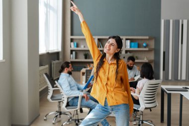 Genç, gülümseyen menajer ekibi açık uzay ofisinde yeni bir proje üzerinde çalışırken ön planda dans ediyor. Takım çalışması konsepti