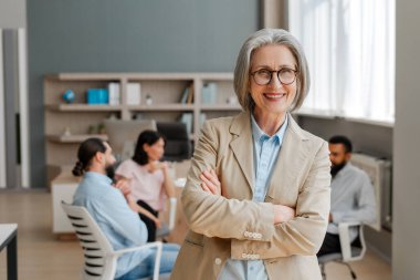 Kendine güvenen kıdemli iş kadını, profesyonellik ve bilgelik saçan bir ekibe liderlik ediyor. Arka planda takım çalışması ve işbirliği görünüyor. Başarılı iş konsepti