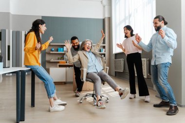 Muhtelif, çok uluslu meslektaşlardan oluşan bir ekip ofisteki başarıyı sevinçle kutluyor, bir iş kadınını sandalyeye oturtup eğleniyor. Takım oluşturma kavramı