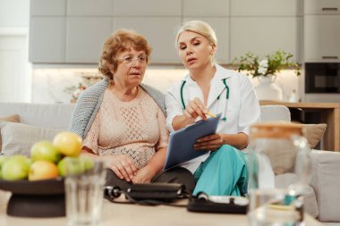 Kadın doktor, ev ziyareti sırasında üst düzey bir hastaya detayları izah ederek güven ve empati bağı kuruyor. Sağlık hizmeti kavramı