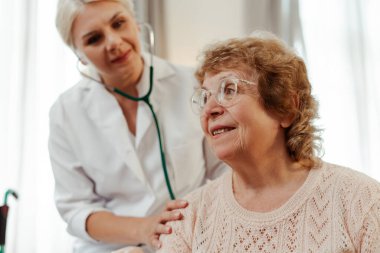 Kadın doktor evde yaşlı bir kadının kalbini ve ciğerlerini dinleyip profesyonel bakım ve destek sağlıyor. Tedavi kavramı