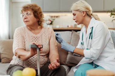 Doktor endişeli yaşlı bir kadını evde aşılıyor, sağlıklı yaşlanma için koruyucu sağlık hizmetlerini vurguluyor. Dokunulmazlık kavramı