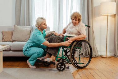 Hemşire yaşlı kadına tekerlekli sandalye, eğitim, rehabilitasyon, iyileşme konseptini kullanmasında yardım ediyor.
