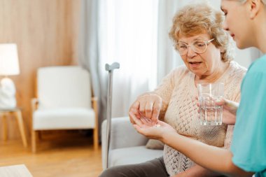 Hemşire yaşlı bir kadına bastonla ilaç veriyor, içme suyu ve haplar, tedavi, sağlık konsepti