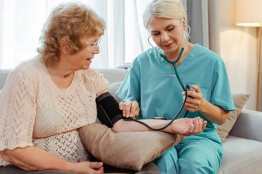 Gülümseyen son sınıf öğrencisi bir kadının kan basıncını evde bir sağlık hemşiresi ölçüyor. Destek. tedavi kavramı