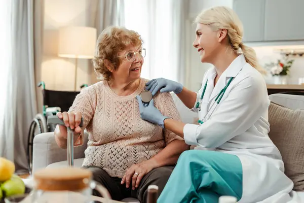 stock image Smiling professional doctor, cardiologist holding pacemaker, showing to senior patient, sitting at home on sofa, explaining. Treatment ICD concept