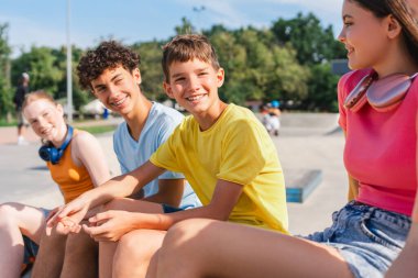 Bir grup gülümseyen arkadaş, renkli tişörtler giyen ve dışarıda konuşan etnik çeşitliliğe sahip gençler. Şehir sokaklarında mutlu stil sahibi kızlar ve erkekler iletişim kuruyor.