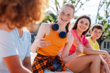 Bir grup gülümseyen arkadaş, renkli tişörtler giyen ve dışarıda konuşan etnik çeşitliliğe sahip gençler. Şehir sokaklarında mutlu stil sahibi kızlar ve erkekler iletişim kuruyor.